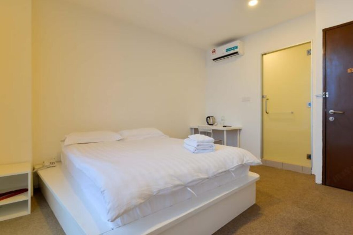 Une chambre avec un lit simple, un lit blanc, une petite table de chevet avec une bouilloire, un climatiseur fixé au mur et une porte sur le côté droit.