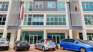 Un moderno edificio de hotel con el letrero “HOTEL DE IDEAL” bien visible. Hay varios coches estacionados en la parte delantera, y el edificio cuenta con amplias ventanas y un diseño contemporáneo y limpio.