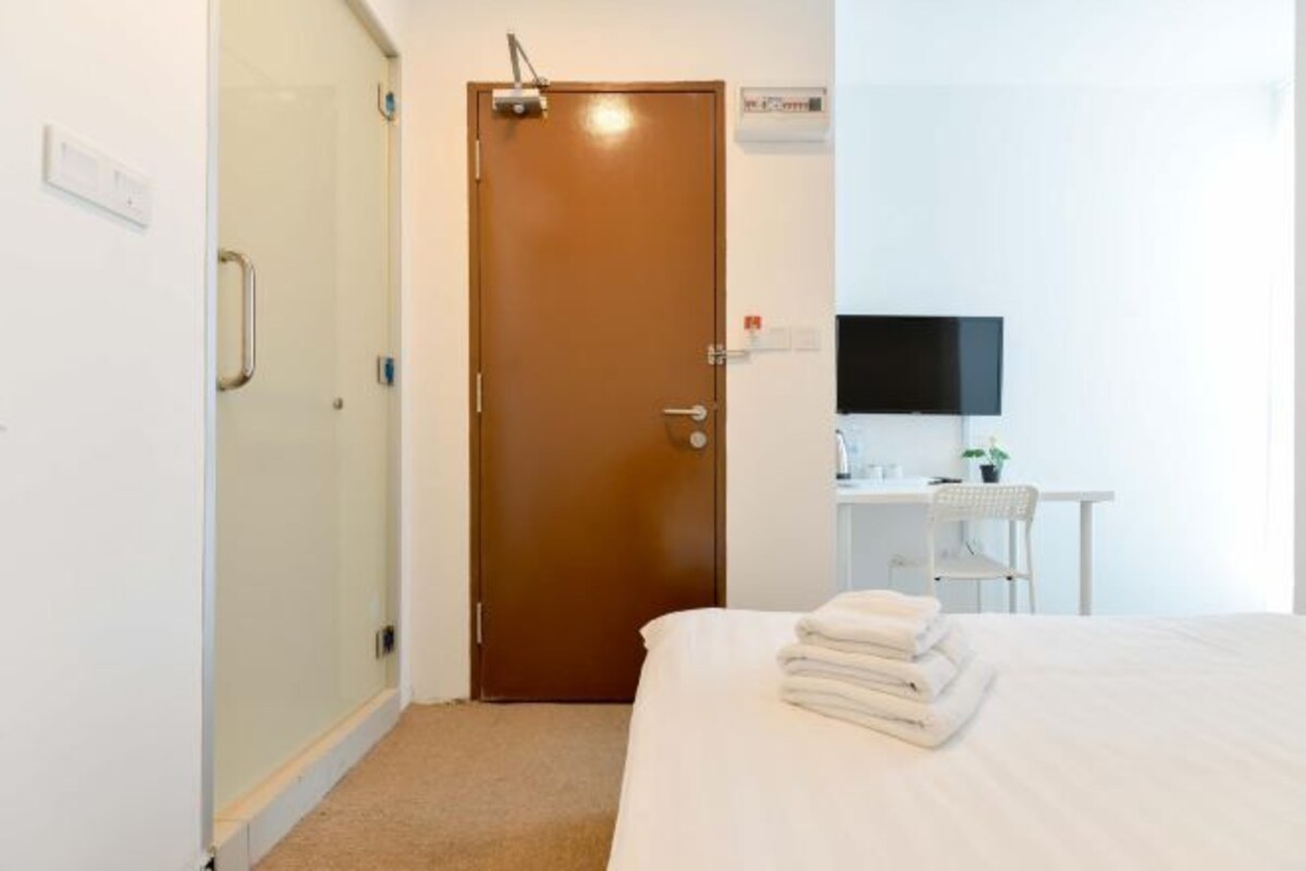 Une chambre d’hôtel avec un lit, un bureau avec un ordinateur, une douche et une porte.