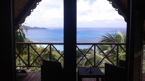 Una terraza de madera con dos sillas y una mesita, con vistas a la costa, el océano y tierra a lo lejos.