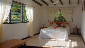 Un dormitorio con una cama, una mesa de madera, una ventana con cortinas y un ventilador de techo.