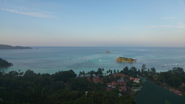 A coastal view with clear waters, boats, and a small island with buildings. - Mango Lodge (Praslin Island)