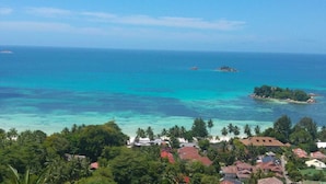 Vista costera con aguas turquesas cristalinas, una pequeña isla y vegetación tropical exuberante.