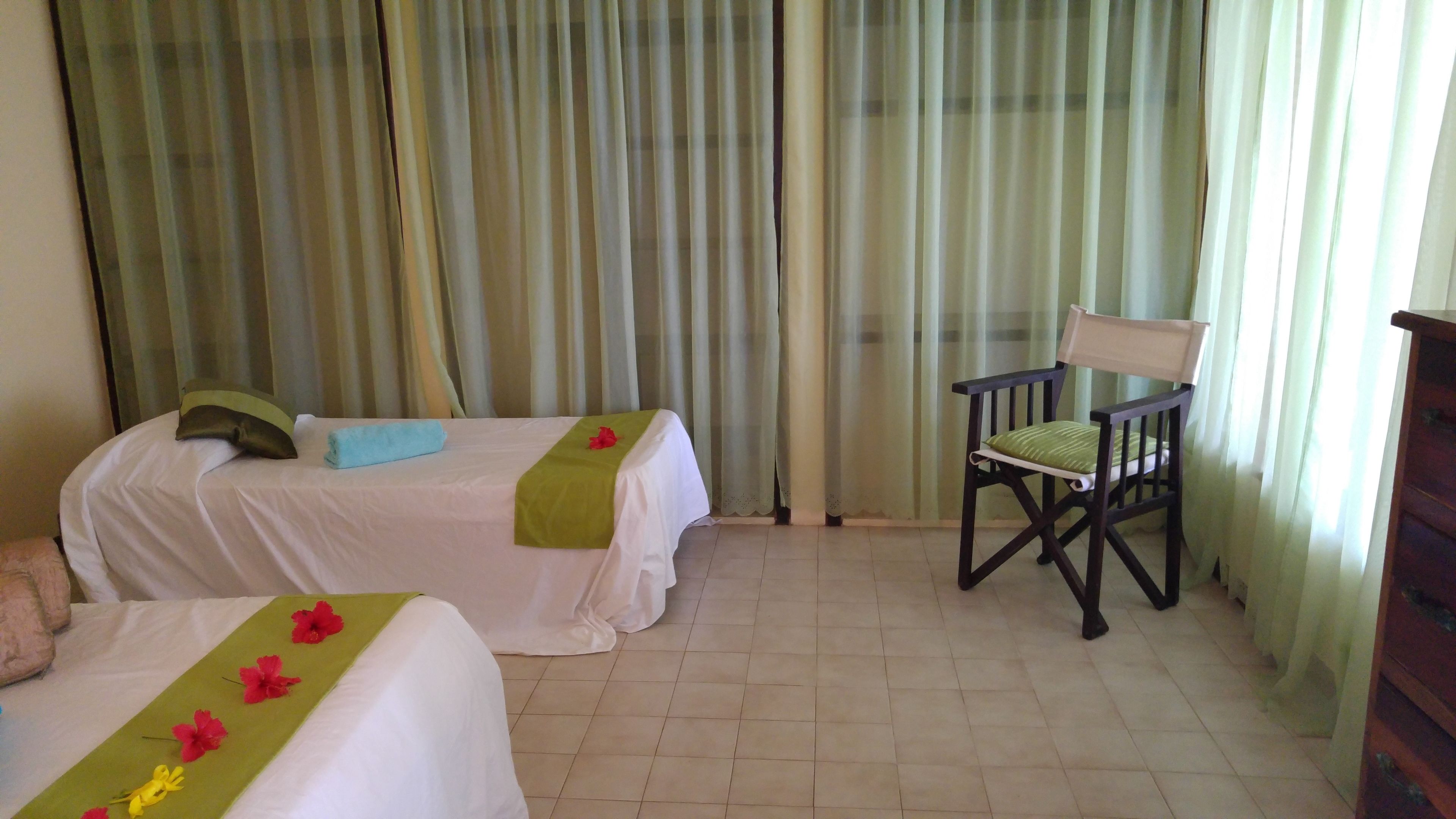 Habitació d'hotel amb dos llits, una cadira i un gran finestral amb cortines.