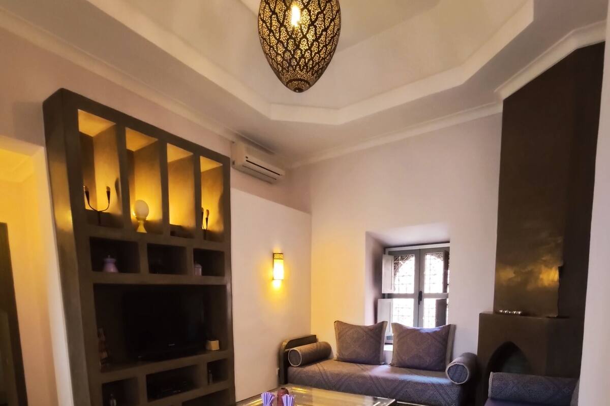 A modern living room with a glass coffee table, a sofa, and a patterned ottoman.