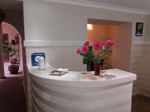 A reception desk with a white counter, a vase with pink flowers, a blue sign, and a white lamp. - Dar Andamaure (Marrakech)