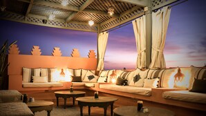 Una zona de estar acogedora con un conjunto de sofás, mesas redondas y un techo decorativo.