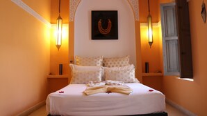 Una cama impecablemente arreglada con sábanas blancas y un arreglo decorativo de almohadas, un cuadro colgado en la pared y dos apliques.