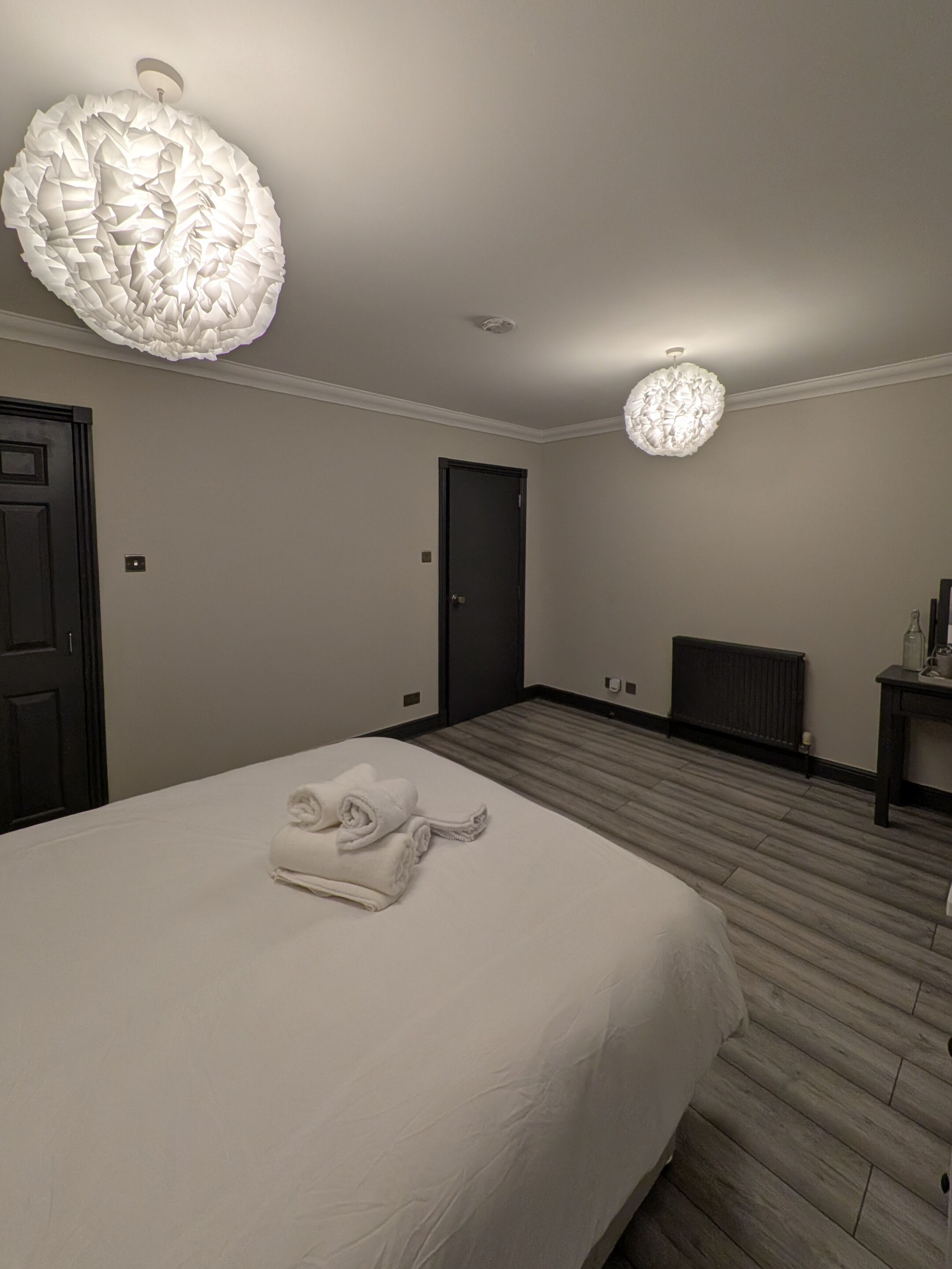 A hotel room with a large bed, a dark door, a radiator, and a wall-mounted light fixture.