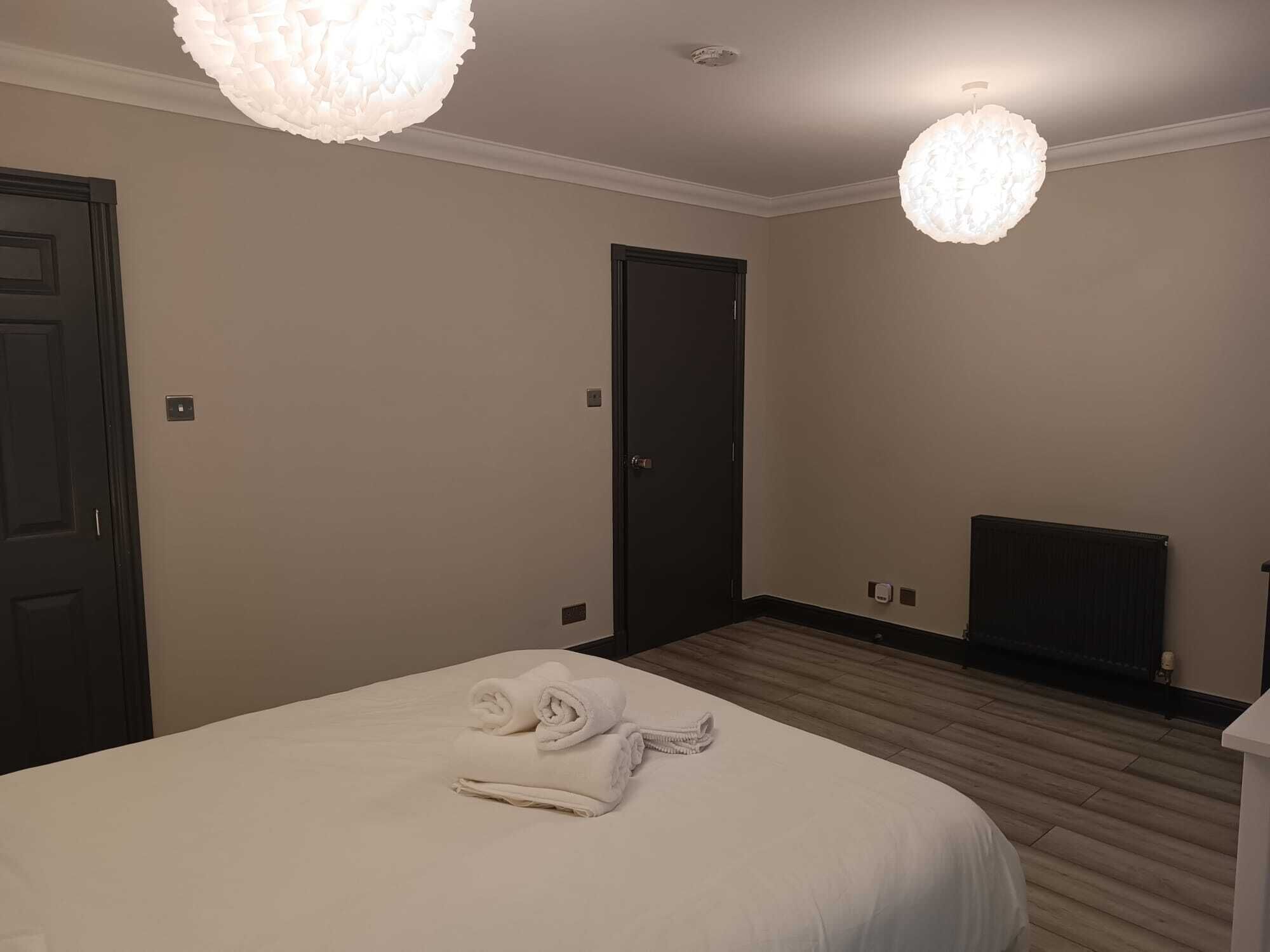 A hotel room with a large bed, two doors, a radiator, and two pendant lights.