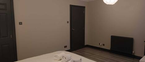 A hotel room with a large bed, two doors, a radiator, and two pendant lights.