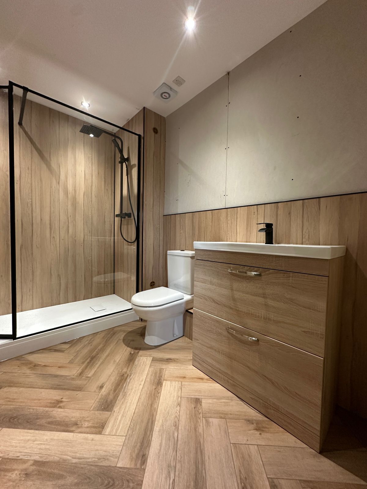 A modern bathroom with a shower enclosure, toilet, and wooden cabinetry.
