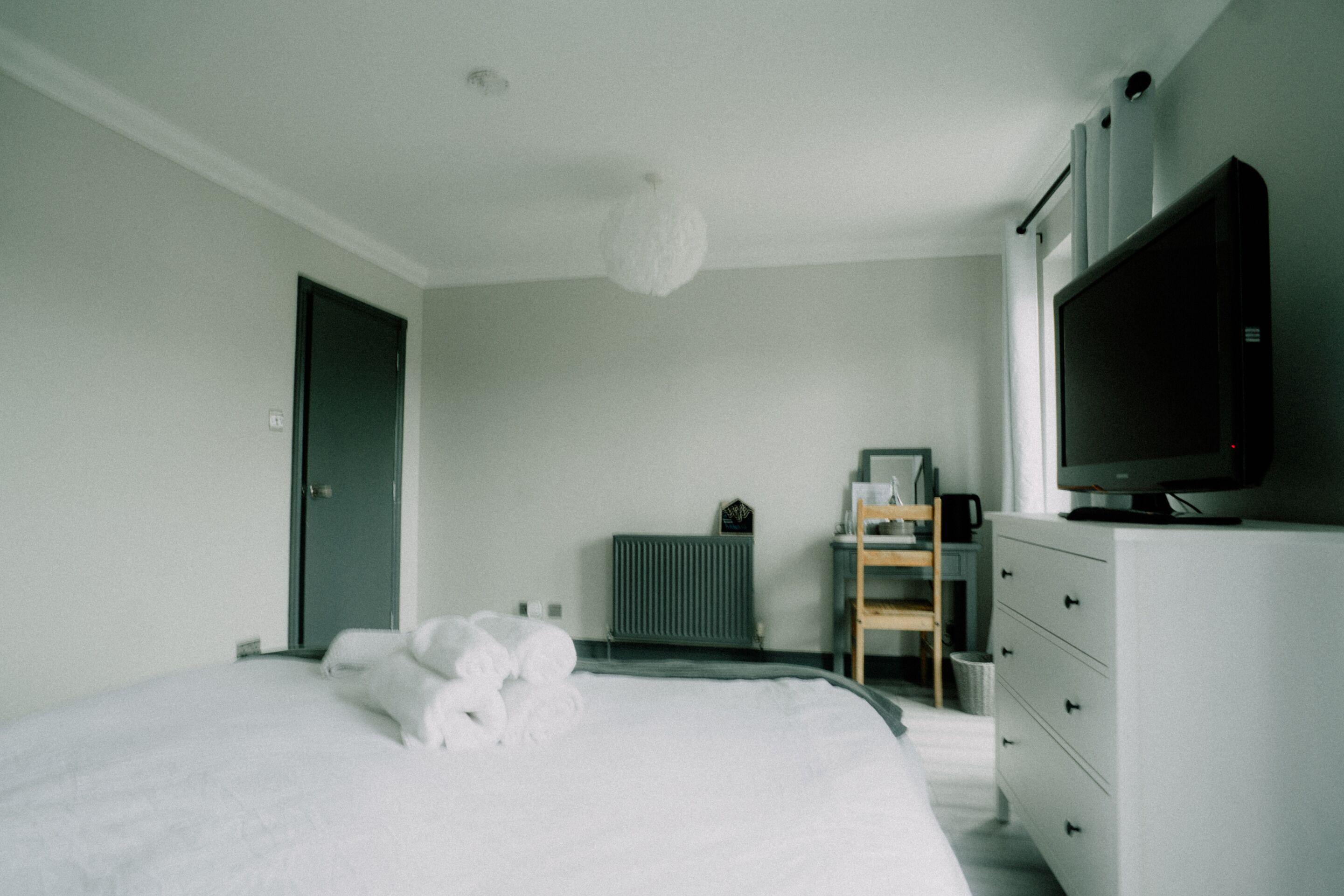 A bedroom with a bed, a dresser, a television, and a radiator.