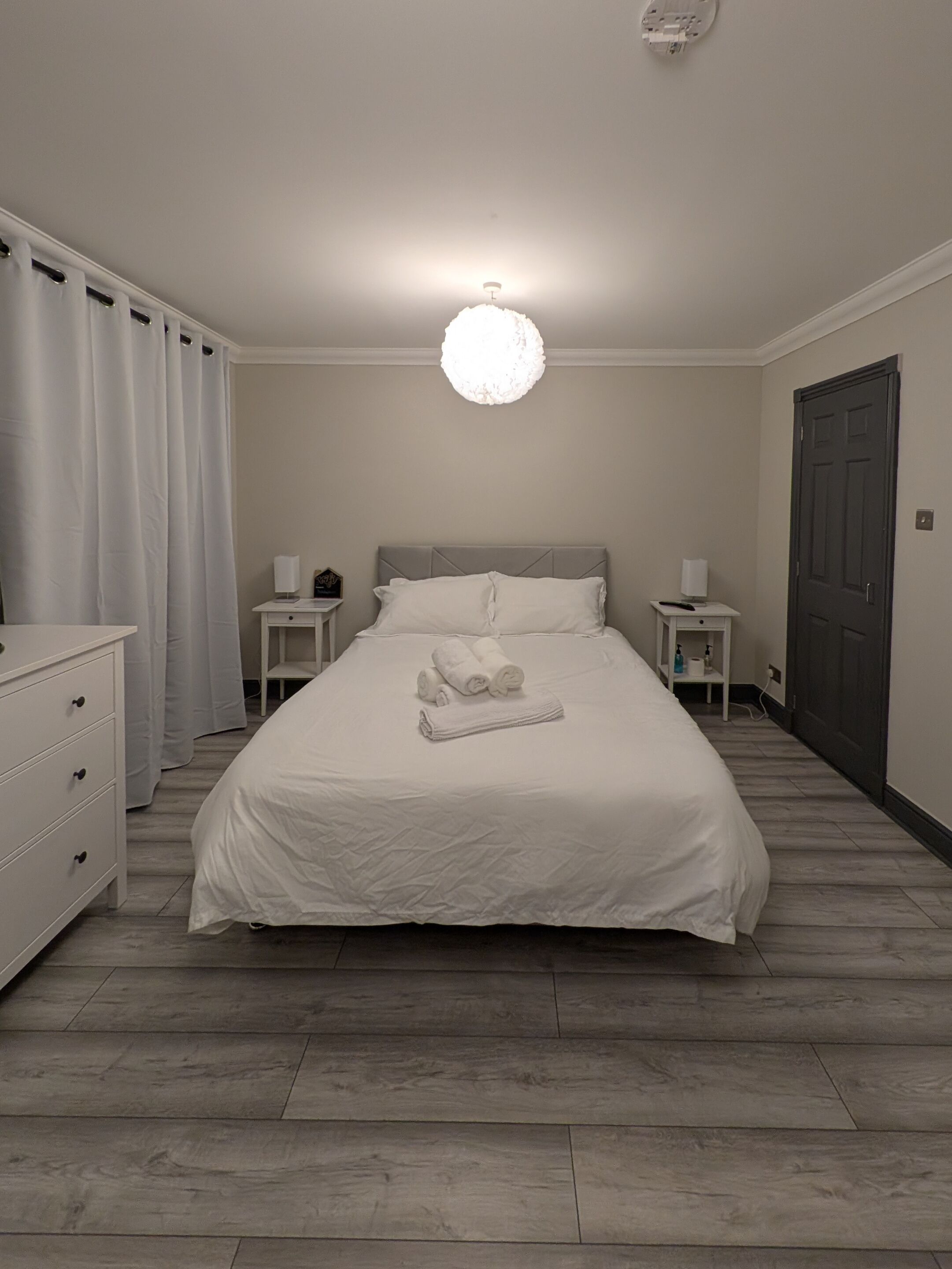 A neatly arranged bedroom with a bed, bedside tables, a dresser, and a door.