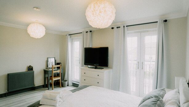 A hotel room with a bed, a television on a dresser, a chair, and a radiator. - Woodgrove Holiday Homes, Inverness (Inverness)