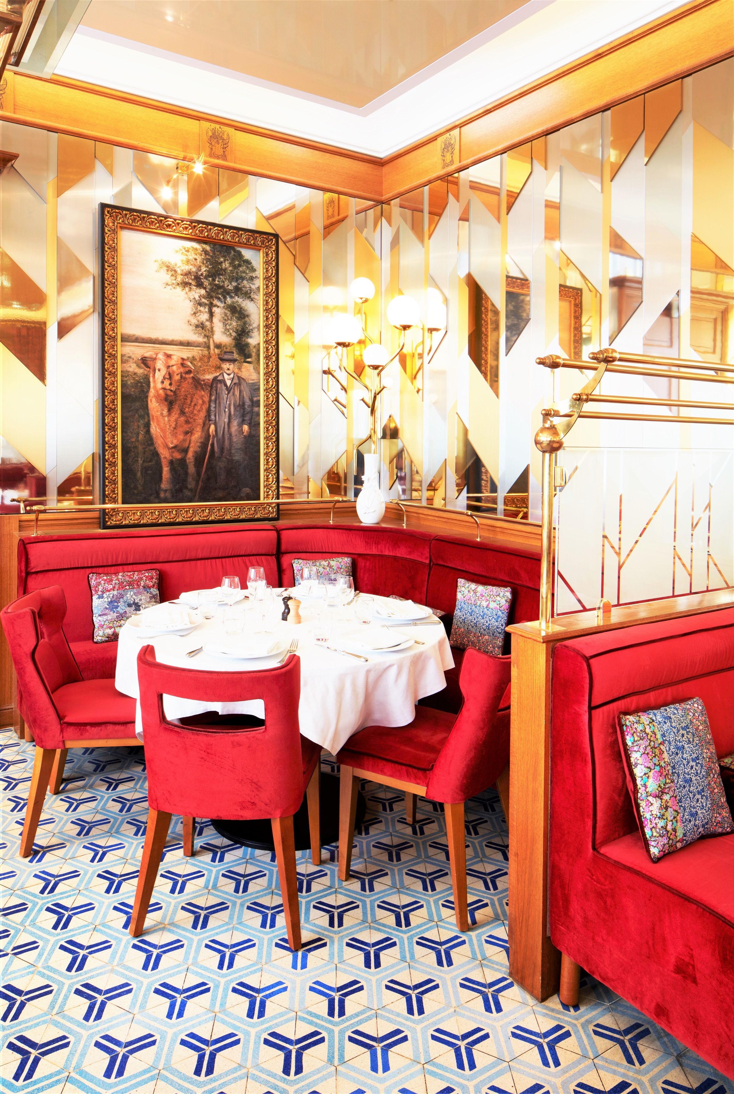 A dining area with red upholstered seating, a white tablecloth, and a large framed painting on the wall.
