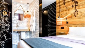 Ein modernes Hotelzimmer mit einem Bett, einem runden Spiegel, einer Holzvertäfelung und einer Wand aus schwarzen Ziegeln.