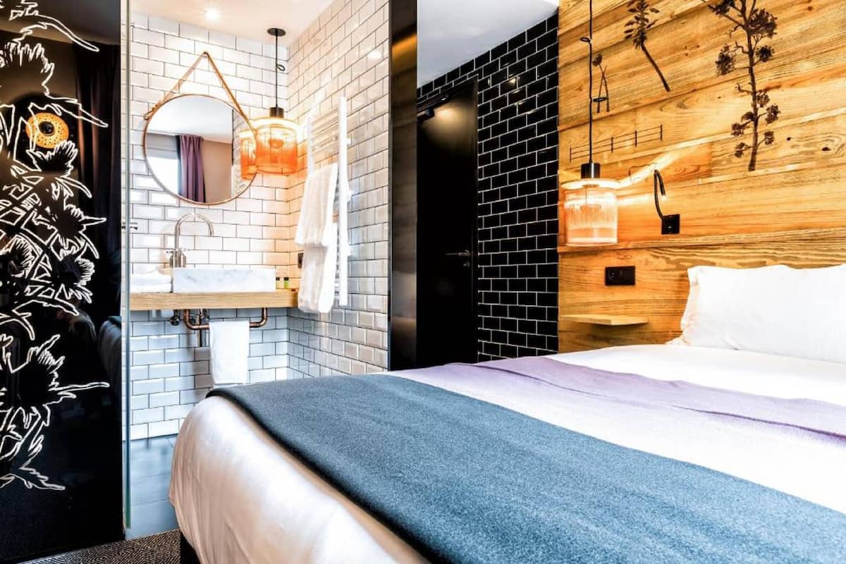 Ein modernes Hotelzimmer mit einem Bett, einem runden Spiegel, einer Holzvertäfelung und einer Wand aus schwarzen Ziegeln.