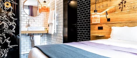 Habitación de hotel moderna con una cama, un espejo redondo, una pared de madera y una pared de ladrillo negro.