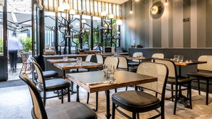 Ein modernes Restaurant mit Holztischen, schwarzen und Korbstühlen sowie Pendelleuchten.