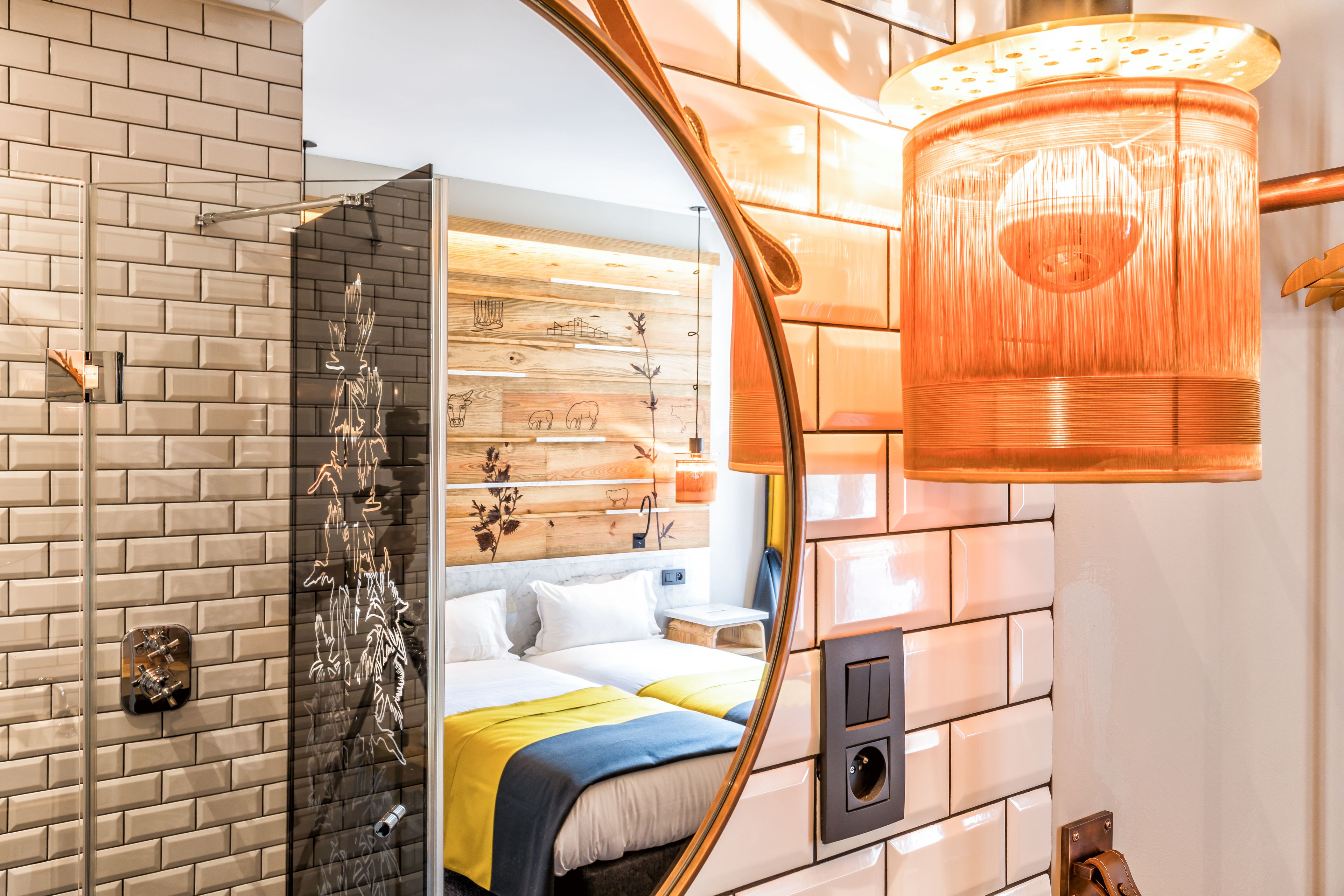 A modern hotel room with a brick wall, wooden panel design, and a large mirror reflecting the bed and bathroom.
