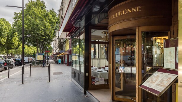 Ein Schaufenster mit einem Schild mit der Aufschrift 'COURONNE' und einer Glastheke mit einer Speisekarte.