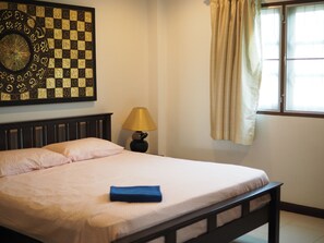 A neatly made bed with a blue towel, a wall clock, and a lamp.