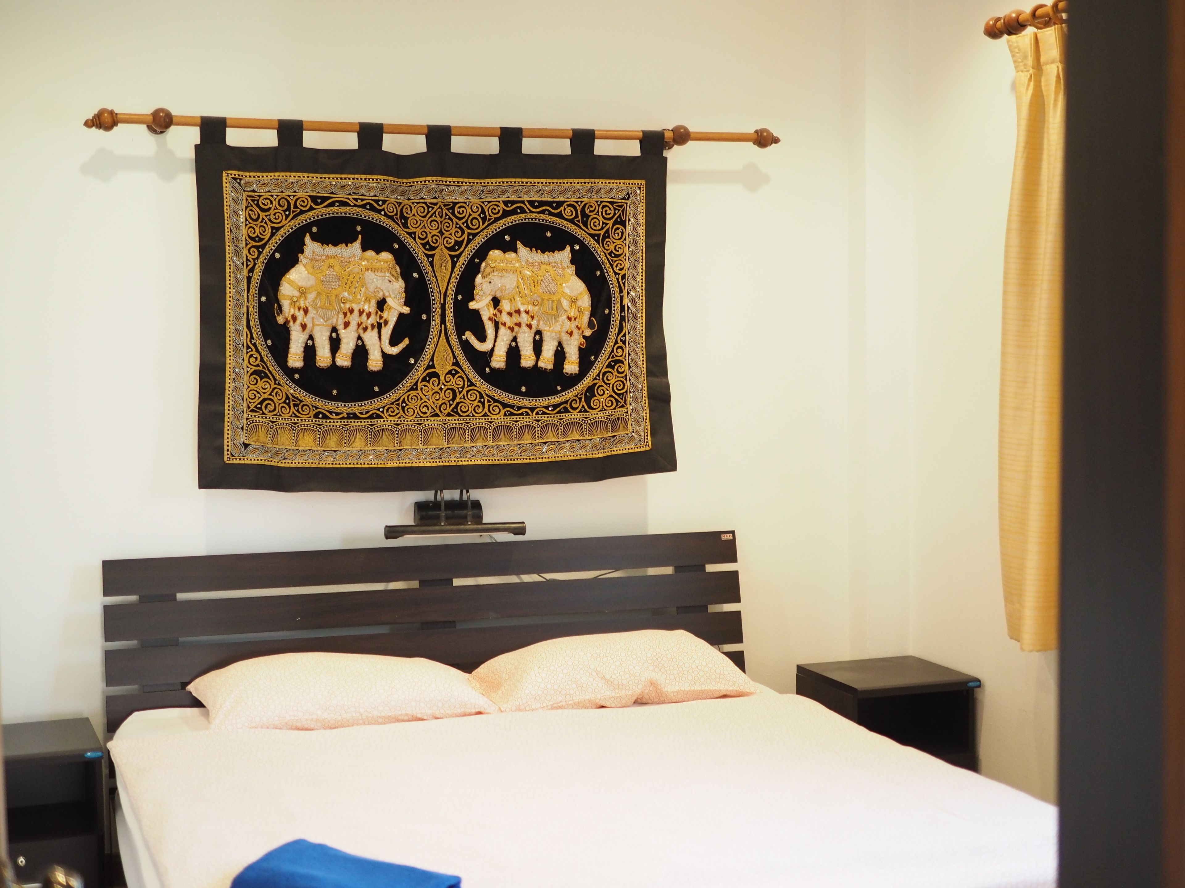 A bed with a headboard, a bedside table, and a wall-mounted tapestry with elephant designs.