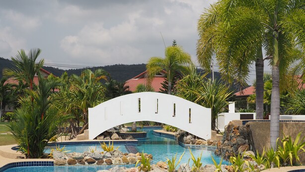 A swimming pool with a white bridge, surrounded by palm trees and rocks.