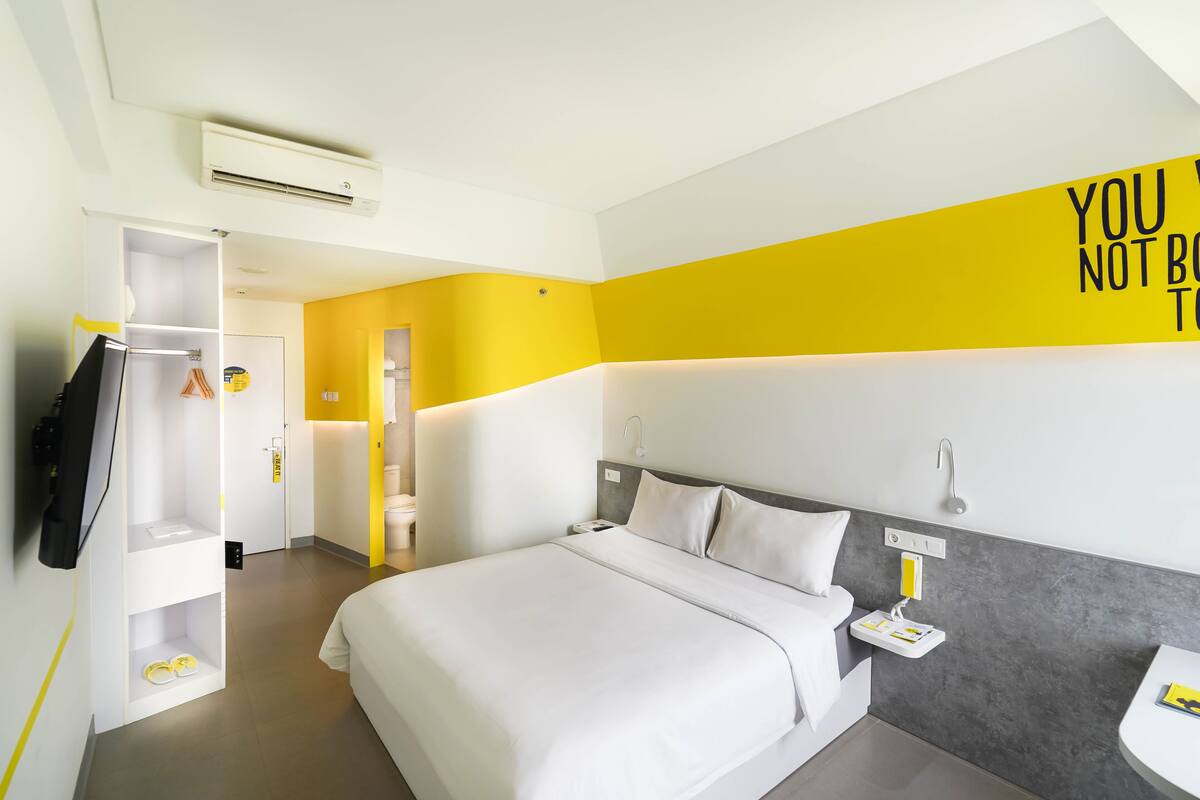 Habitación de hotel con cama, armario, mesita de noche y una pared con una cita motivacional.