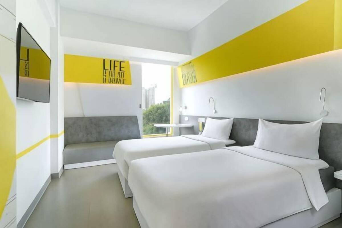 Una habitación de hotel moderna con dos camas, un televisor, una mesita pequeña y una ventana con vistas.
