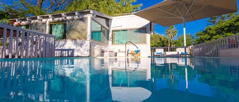 Una piscina al aire libre, sombrillas, sillones reclinables de piscina