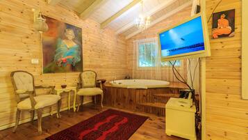 A wooden cabin interior with a large painting, a television, a hot tub, and a red patterned rug.