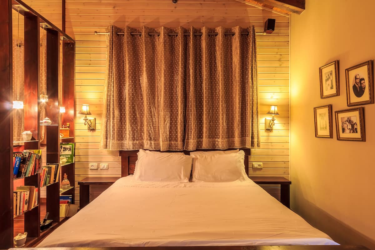 A neatly made bed with white linens, a bookshelf filled with books, and a curtain with a polka dot pattern.