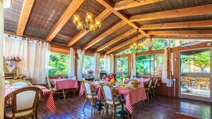An indoor dining area with wooden beams, red and white checkered tablecloths, wicker chairs, and hanging light fixtures. - Betzel Haella (Mevoot HaHermon)