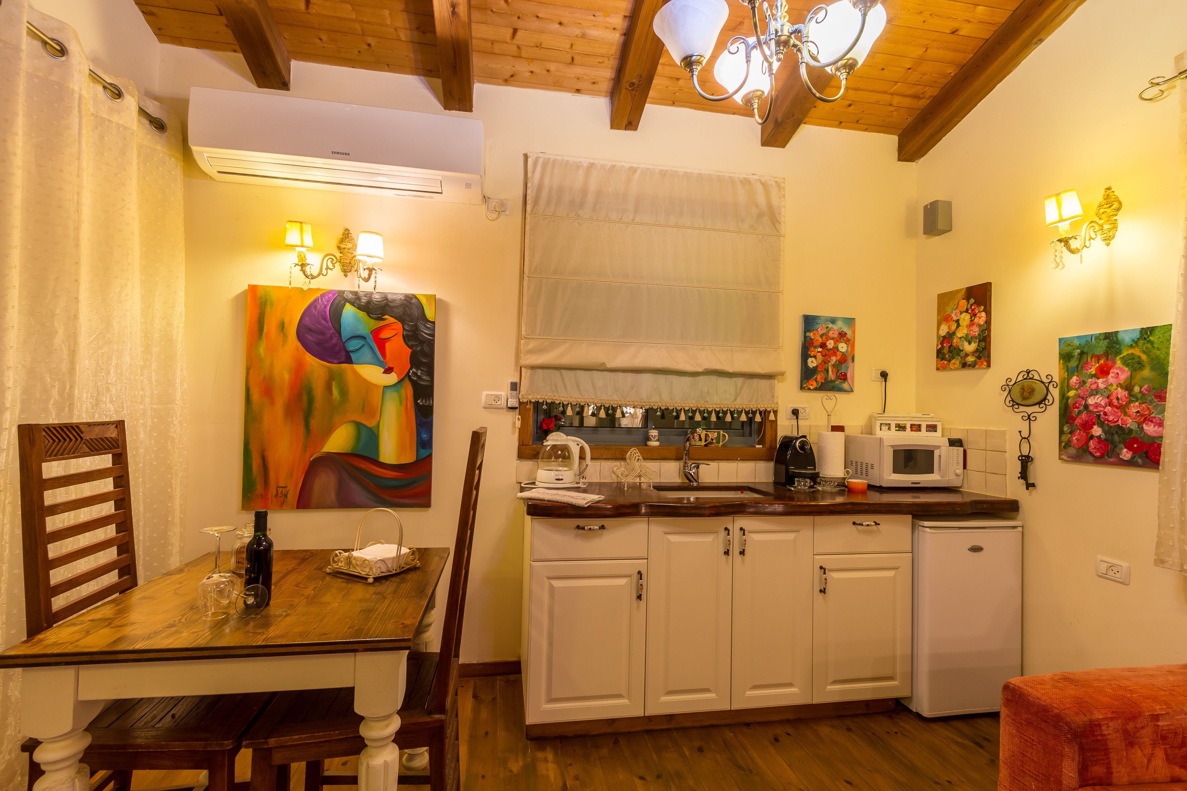 A compact kitchen with white cabinets, a wooden dining table, and a small refrigerator.