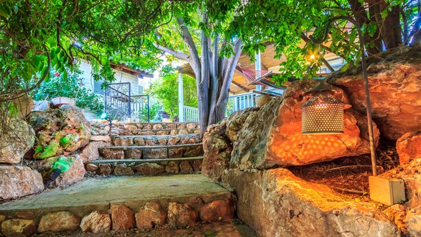 A stone staircase leading up to a wooden deck, surrounded by lush greenery and a lantern. - Betzel Haella (Mevoot HaHermon)