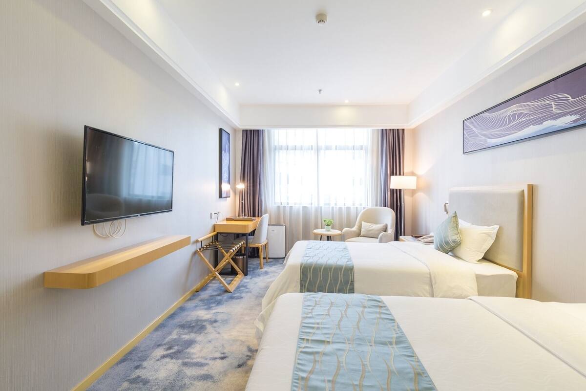 Habitación de hotel con dos camas, un escritorio, una silla, un televisor y una ventana con cortinas.