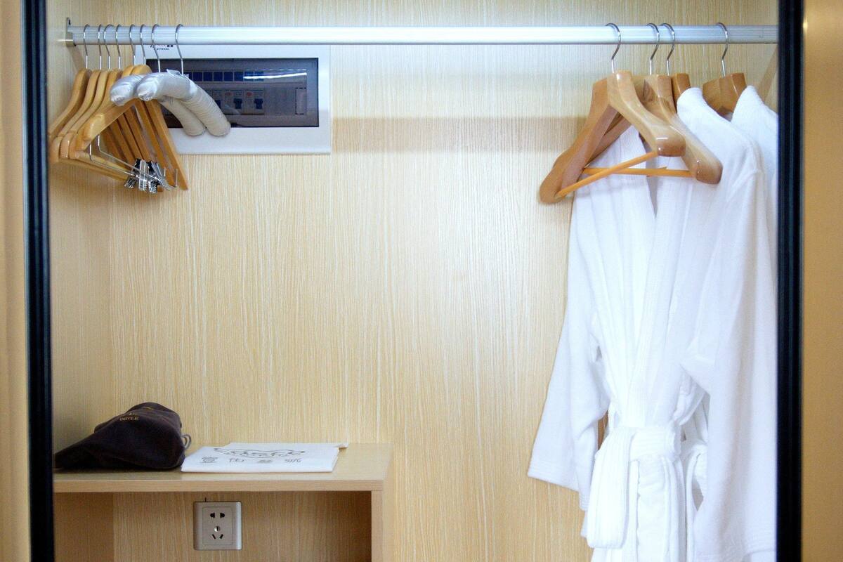Habitación de hotel con un armario de madera que contiene una bata blanca, un perchero de madera y un pequeño electrodoméstico blanco.