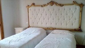 Quarto com duas camas de solteiro, cada uma com edredom branco e cabeceira com design acolchoado.