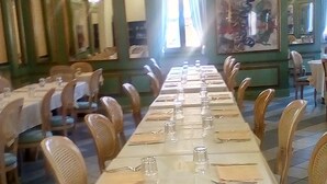 Uma longa mesa de jantar posta para refeição em restaurante, com cadeiras em ambos os lados.