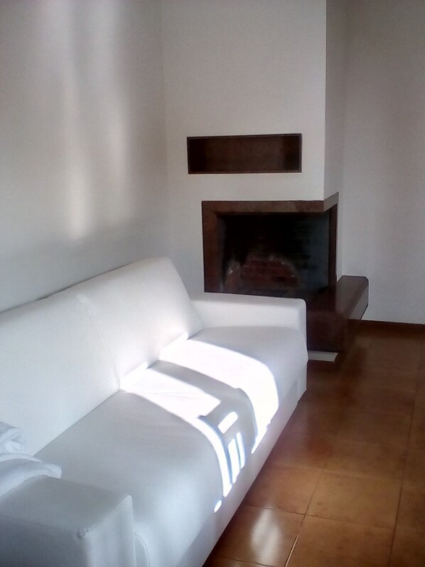 A modern living room with a white sofa, a fireplace, and a wooden shelf. - Locanda I Tarocchi (Vailate)