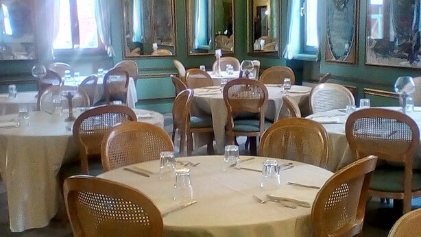 Uma sala de jantar com mesas e cadeiras redondas, piso de azulejos e grandes espelhos nas paredes.