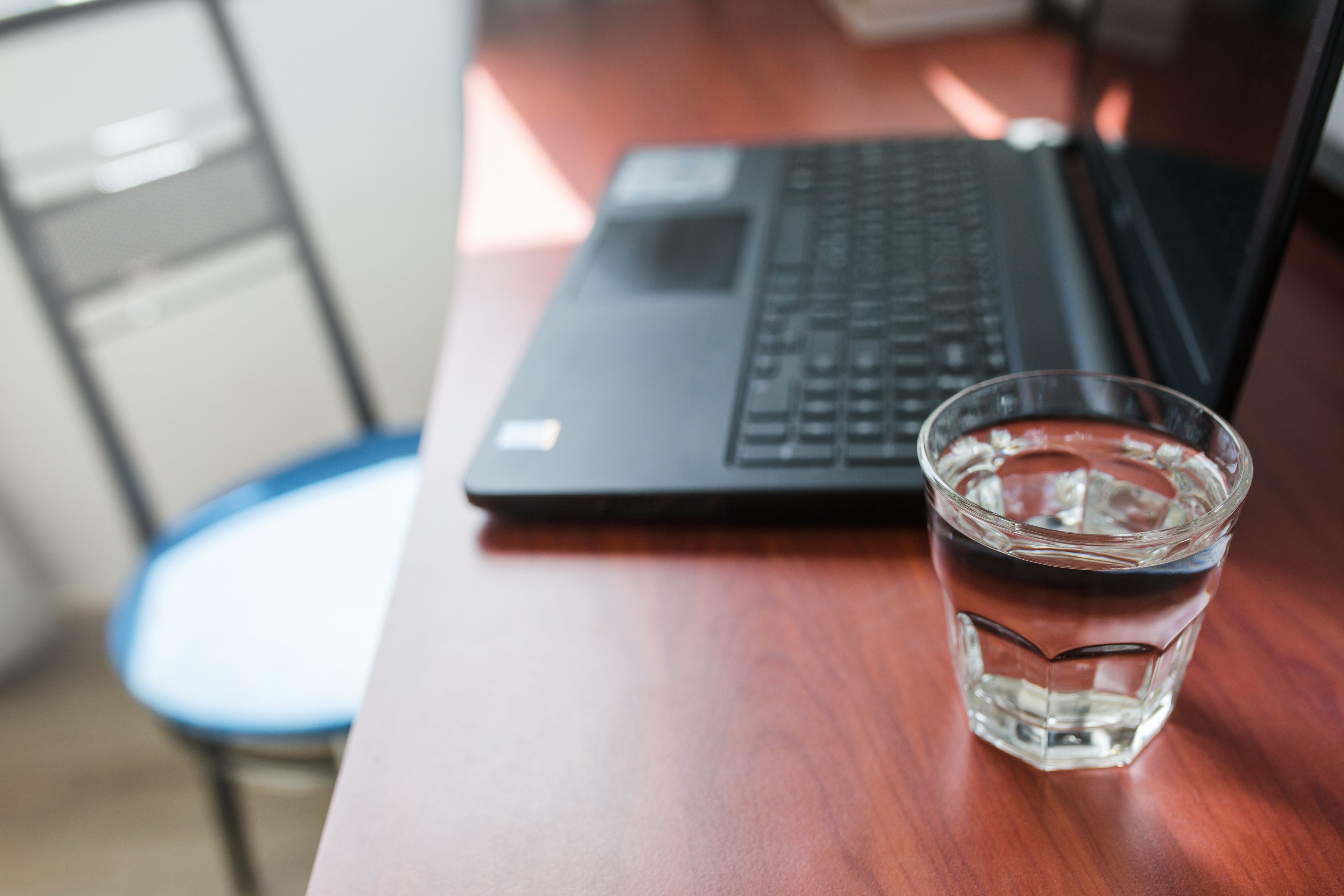 A laptop and a glass of water on a wooden desk.