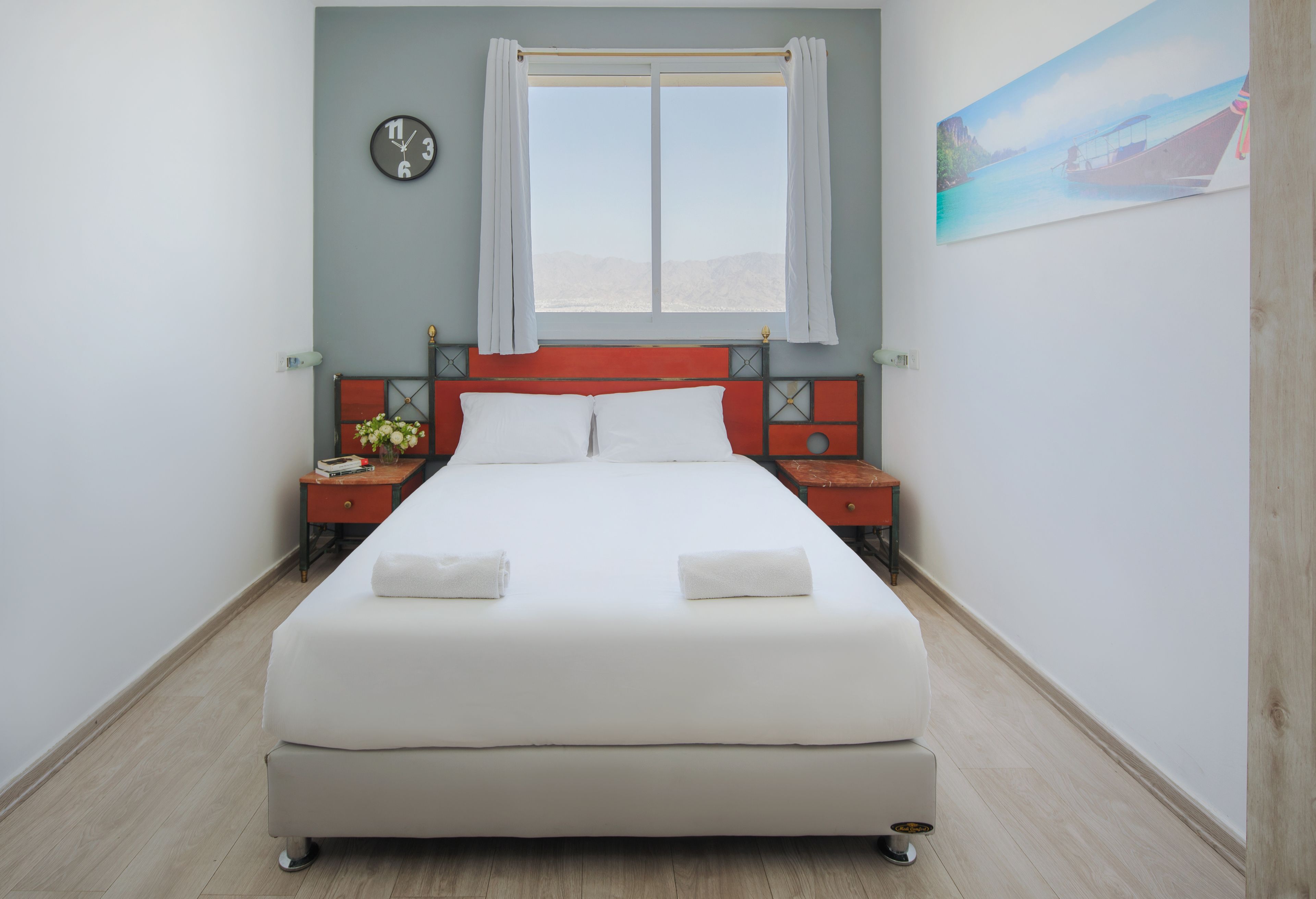Une chambre bien rangée, avec un lit, des tables de chevet, une horloge et une fenêtre avec des rideaux.