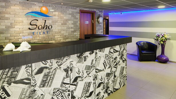 A reception area with a brick wall, a wooden door, and a counter with newspaper clippings. - Soho Eilat (Eilat)