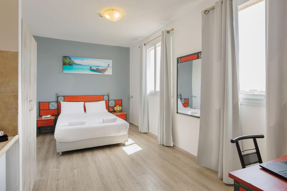 Une chambre d’hôtel avec un lit, un bureau avec un ordinateur portable, une fenêtre avec des rideaux, un tableau au mur et une vue sur la ville.