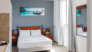 A hotel room with a large bed, a nightstand with a vase of flowers, a painting of a boat on the wall, and a window with curtains. - Soho Eilat (Eilat)