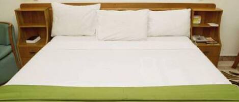 A neatly made bed with white linens and a green throw blanket, flanked by wooden nightstands with lamps.