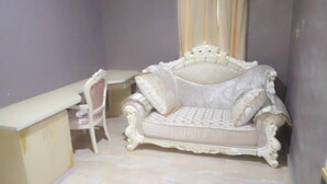 A room with a white ornate sofa, a small chair, and a white desk.